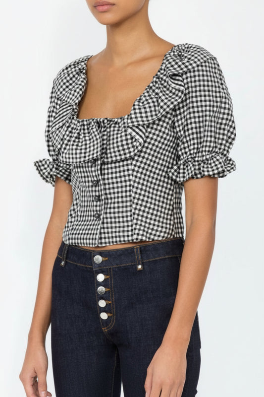 Person wearing a black and white checkered blouse with puffed sleeves on a plain background
